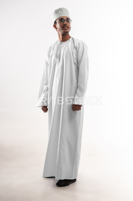 Expressions of intelligence and cleverness, the concept of elegance and interest in external appearance, a portrait of a young Arab Gulf Omani man wearing a dishdasha, a sleeve and eyeglasses, looking at something with gestures of focus and precision, a full-length body image, white background