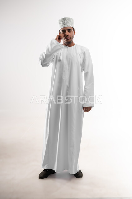 التهاب الأنف التحسسي, الشعور بالمرض و الزكام والحاجة الى العلاج والدواء, بورتريه لشاب عربي خليجي عماني يرتدي الدشداشة و الكمه ينظر الى الكاميرا يضع يده على أنفه بإيماءات التعب و الألم, صورة الجسم بالطول الكامل، خلفية بيضاء