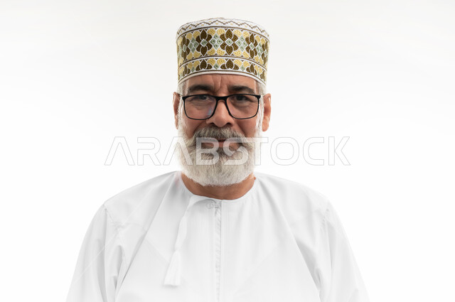 Looking at the camera with gestures of pleasure and cheerfulness, interest in outward appearance, concept of masculinity and dignity, close-up portrait of an elderly Arab Gulf Omani man wearing the traditional dishdasha, Omani kummah and eyeglasses standing with an expression of self-confidence, white background