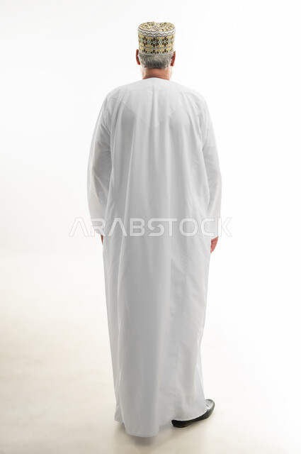 Concern for appearance, concept of prestige and dignity, appreciation and respect for elderly men, portrait from behind of an old Arab Gulf Omani man wearing a dishdasha and traditional Omani kummah standing straight, full body, white background