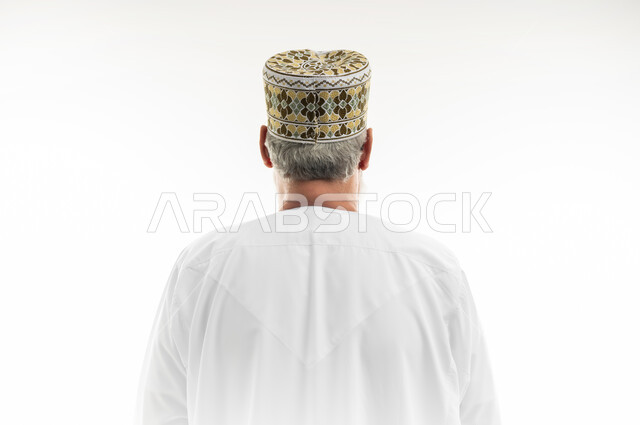 مفهوم الهيبة والوقار، الاهتمام بالمظهر الخارجي، تقدير الرجال كبار السن واحترامهم، بورتريه مقرب من الخلف لرجل شايب عربي خليجي عماني يرتدي الدشداشة والكمه العمانية التقليدية يقف بشكل مستقيم، خلفية بيضاء