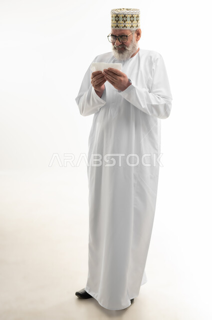 العطاس والكحه وأعراض الرشح، الإصابة بالزكام والانفلونزا، بورتريه لرجل شايب عربي خليجي عماني يرتدي الدشداشة والكمه العمانية يمسك المنديل الورقي بيده لمنع انتشار العدوى، الإرهاق والتعب والحاجة للراحة، ضرورة أخذ العلاج المناسب، الجسم بالطول الكامل، خلفية بيضاء