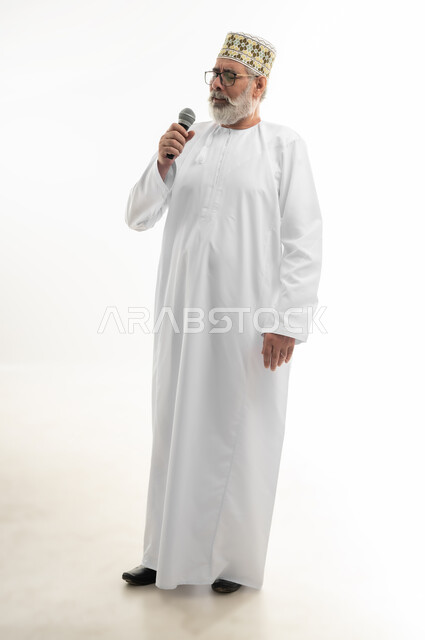 إلقاء المحاضرات وإقامة الندوات، الدورات التدريبية و ورشات العمل، تبادل الحوار والاستفادة من خبرات كبار السن، بورتريه لرجل شايب عربي خليجي عماني يرتدي الدشداشة والكمه والنظارة الطبية يحمل مكبر الصوت بيده ويقوم بالنقاشات الهامة، الجسم بالطول الكامل، خلفية بيضاء