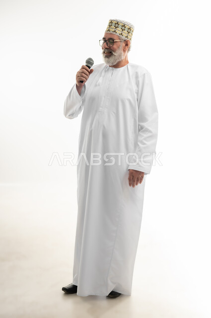 تبادل الحوار والاستفادة من خبرات كبار السن، الدورات التدريبية و ورشات العمل، إلقاء المحاضرات وإقامة الندوات، بورتريه لرجل شايب عربي خليجي عماني يرتدي الدشداشة والكمه والنظارة الطبية يحمل مكبر الصوت بيده ويقوم بالنقاشات الهامة، الجسم بالطول الكامل، خلفية بيضاء