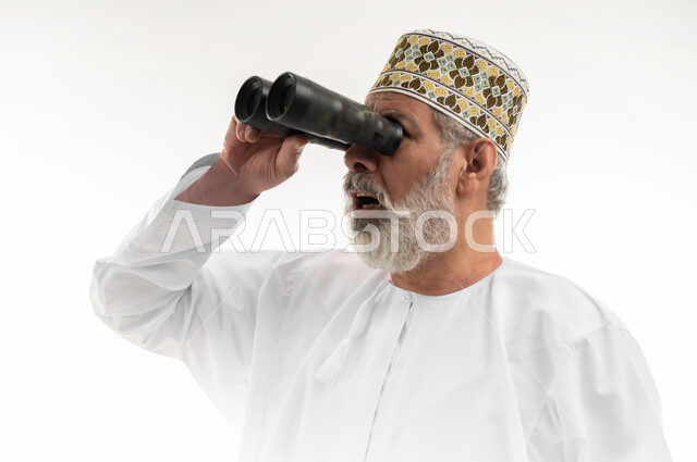 Planning for future goals, seeing distant objects using a telescope, love of adventure and exploration, close-up portrait of an elderly Arab Gulf Omani man wearing the traditional dishdasha and Omani kummah, putting his hand on his forehead and looking through binoculars, white background