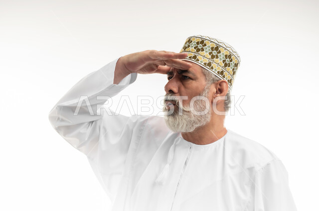 إيماءات التركيز للحصول مشاهدة واضحة،محاولة رؤية الأشياء البعيدة،  بورتريه مقرب لرجل كبير بالسن عربي خليجي عماني يرتدي الدشداشة التقليدية والكمه العمانية يضع يده فوق جبينه وينظر إلى اتجاه معين، خلفية بيضاء