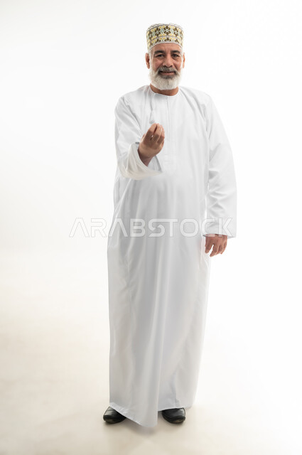 Hand gesture indicating deliberation, requesting to take it easy on something, portrait of an old Arab Gulf Omani man wearing the traditional Omani dishdasha and kummah, standing straight and looking at the camera with gestures of pleasure and cheerfulness, full body, white background