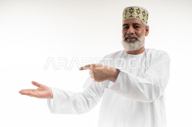 الاهتمام بالمظهر الخارجي، الإشارة بالاصبع إلى شيء ما بإيماءات السرور، بورتريه مقرب لرجل شايب عربي خليجي عماني يرتدي الدشداشة والكمه العمانية التقليدية يقف بشكل مستقيم ويحمل بيده عنصر وهمي، خلفية بيضاء