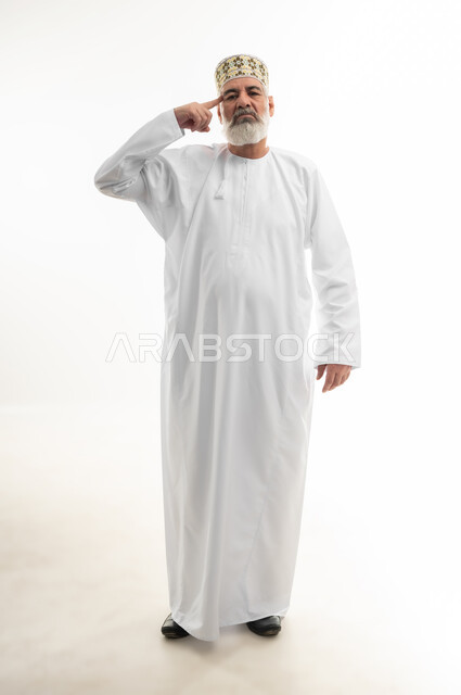 الإشارة إلى العقل والتفكير بحكمة، الحرية الشخصية والثقة بالنفس، بورتريه لرجل شايب عربي خليجي عماني يرتدي الدشداشة والكمه العمانية التقليدية يقف بشكل مستقيم وينظر إلى الكاميرا بإيماءات السرور والسعادة، الجسم بالطول الكامل، خلفية بيضاء