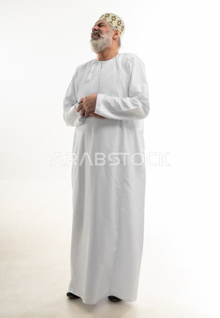 ضرورة أخذ الدواء للتعافي من المرض، إمساك البطن والشعور بآلام المغص، بورتريه لرجل كبير بالسن عربي خليجي عماني يرتدي الدشداشة والكمه يضع يديه على معدته بإيماءات الاضطراب والانزعاج، أهمية زيارة الطبيب والحصول على قسط من الراحة، الجسم بالطول الكامل، خلفية بيضاء