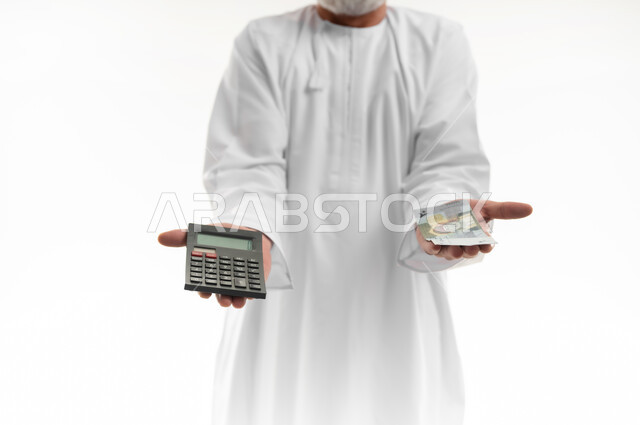 الأعمال الاقتصادية المالية، محاولة إدارة المصروف المنزلي بتدبر، بورتريه مقرب ليدي لرجل كبير بالسن عربي خليجي عماني يرتدي الدشداشة والكمه العمانية التقليدية يمسك بإحدى يديه الحاسبة الرقمية باليد الأخرى مجموعة من النقود، السعي نحو التوفير والادخار، خلفية بيضاء