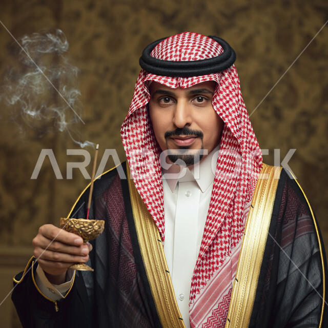  التطيب بالعود والبخور, صورة مقربة لشاب عربي خليجي سعودي مبتسم يرتدي الشماغ والثوب التقليدي والبشت ينظر إلى الكاميرا ويحمل المبخرة, الأناقة والاهتمام بالمظهر الخارجي, العادات والتقاليد السعودية, 