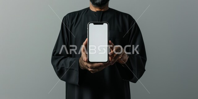 استخدام أجهزة التكنولوجيا الحديثة والمتطورة، بورتريه لرجل عربي خليجي سعودي يحمل هاتف محمول, عرض شاشة بيضاء فارغة عبر الجوال, متاجر تسوق الكترونية، خلفية رمادية