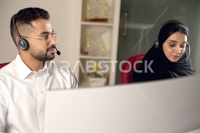 Two Saudi Arabian Gulf employees working in customer service, an employee and an employee wearing a headset, making inquiries and inquiries, answering customer questions, making video calls through a computer, following up and developing work