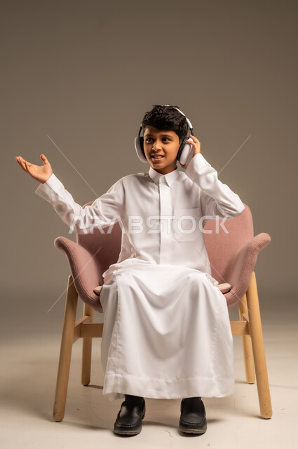 استخدام تقنية الهيدفون، الاستماع الى الأغاني والموسيقى عبر سماعة الرأس، بورتريه مقرب لطفل عربي خليجي سعودي يضع سماعة الرأس يقوم بالإصغاء والاستماع إلى شيء ما، خلفية بيج