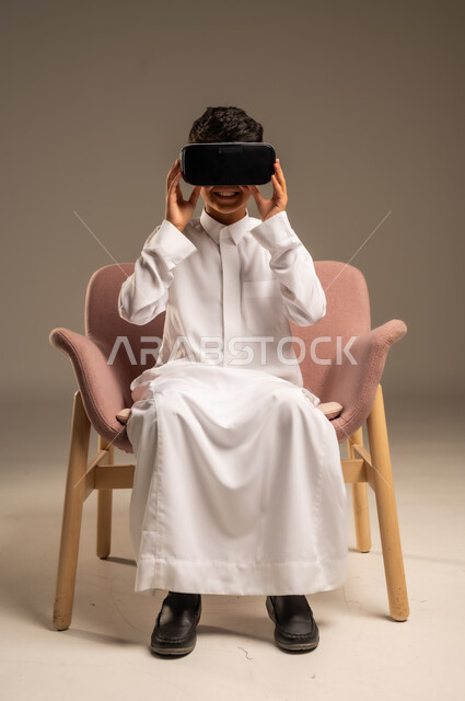 إيماءات التفاعل والاندماج، تطورأساليب التعليم باستخدام التقنيات الحديثة ومحاكاة العالم الخيالي، بورتريه لولد عربي خليجي سعودي يرتدي الثوب التقليدي يلبس نظارة الواقع الإفتراضي ثلاثية الأبعاد, خلفية بيج