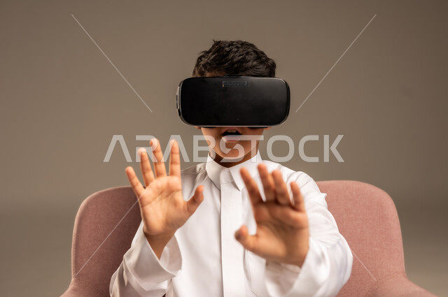 إيماءات التفاعل والاندماج، تطورأساليب التعليم باستخدام التقنيات الحديثة ومحاكاة العالم الخيالي، بورتريه لولد عربي خليجي سعودي يرتدي الثوب التقليدي يلبس نظارة الواقع الإفتراضي ثلاثية الأبعاد, خلفية بيج