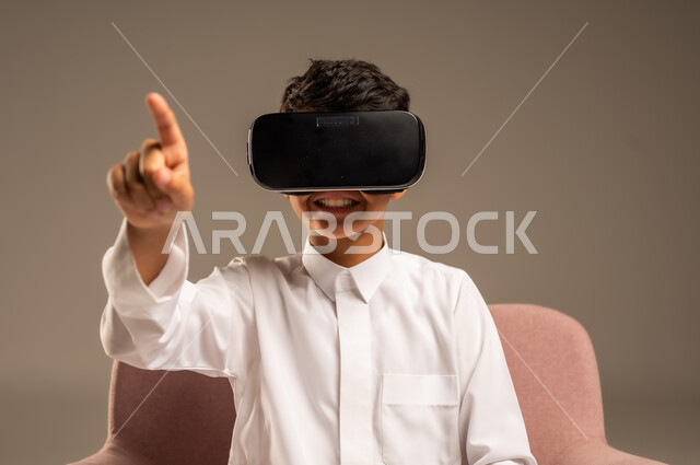 Gestures of interaction and integration, development of teaching methods using modern technologies and simulation of the imaginary world, portrait of a Saudi Arabian Gulf boy wearing traditional dress wearing 3D virtual reality glasses, beige background