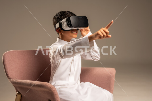 إيماءات التفاعل والاندماج، تطورأساليب التعليم باستخدام التقنيات الحديثة ومحاكاة العالم الخيالي، بورتريه لولد عربي خليجي سعودي يرتدي الثوب التقليدي يلبس نظارة الواقع الإفتراضي ثلاثية الأبعاد, خلفية بيج