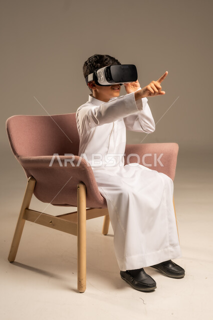 إيماءات التفاعل والاندماج، تطورأساليب التعليم باستخدام التقنيات الحديثة ومحاكاة العالم الخيالي، بورتريه لولد عربي خليجي سعودي يرتدي الثوب التقليدي يلبس نظارة الواقع الإفتراضي ثلاثية الأبعاد, خلفية بيج