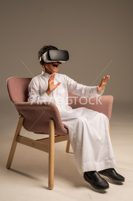 إيماءات التفاعل والاندماج، تطورأساليب التعليم باستخدام التقنيات الحديثة ومحاكاة العالم الخيالي، بورتريه لولد عربي خليجي سعودي يرتدي الثوب التقليدي يلبس نظارة الواقع الإفتراضي ثلاثية الأبعاد, خلفية بيج