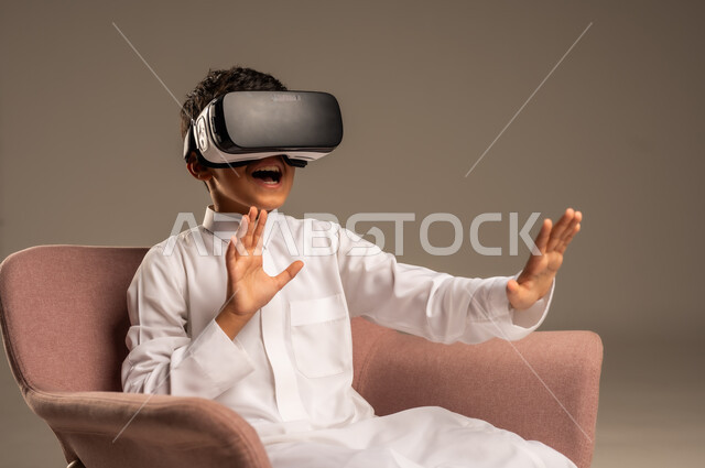 إيماءات التفاعل والاندماج، تطورأساليب التعليم باستخدام التقنيات الحديثة ومحاكاة العالم الخيالي، بورتريه لولد عربي خليجي سعودي يرتدي الثوب التقليدي يلبس نظارة الواقع الإفتراضي ثلاثية الأبعاد, خلفية بيج