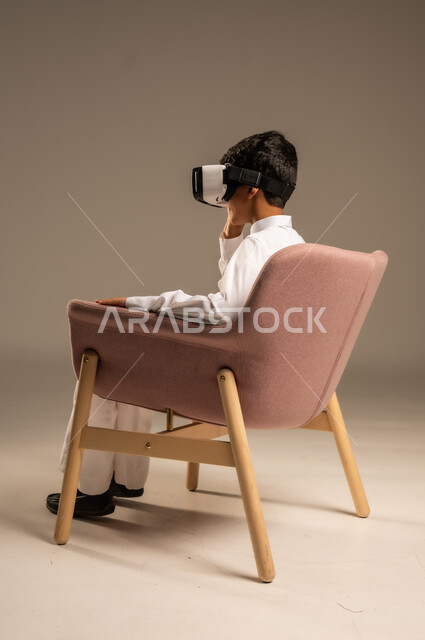 إيماءات التفاعل والاندماج، تطورأساليب التعليم باستخدام التقنيات الحديثة ومحاكاة العالم الخيالي، بورتريه لولد عربي خليجي سعودي يرتدي الثوب التقليدي يلبس نظارة الواقع الإفتراضي ثلاثية الأبعاد, خلفية بيج