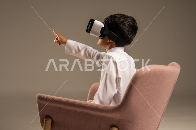إيماءات التفاعل والاندماج، تطورأساليب التعليم باستخدام التقنيات الحديثة ومحاكاة العالم الخيالي، بورتريه لولد عربي خليجي سعودي يرتدي الثوب التقليدي يلبس نظارة الواقع الإفتراضي ثلاثية الأبعاد, خلفية بيج