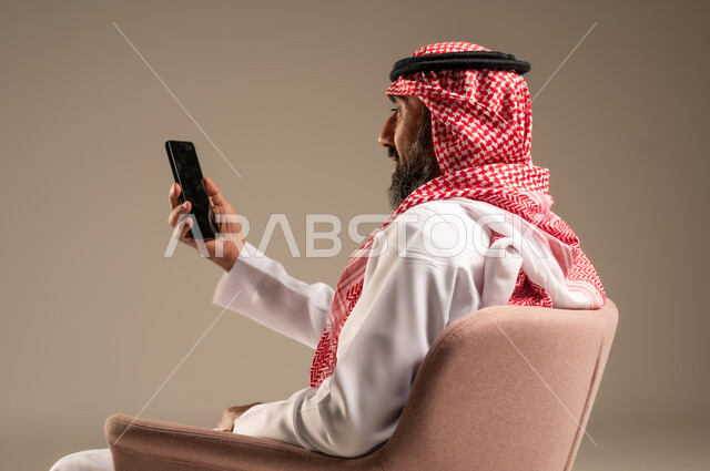 اتصالات ومكالمات هاتفية عبر الهاتف المحمول , الدردشة والتواصل مع الأهل والأصدقاء ، بورتريه لرجل عربي خليجي سعودي يرتدي الثوب التقليدي والشماغ ويستخدم الجوال، خلفية بيج
