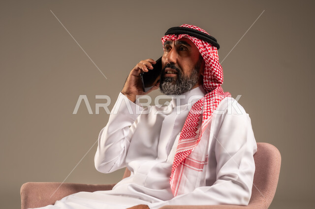 التحدث مع الأصدقاء عبر الجوال، التواصل مع العالم بسهولة، بورتريه لرجل عربي سعودي خليجي كبير بالسن يرتدي الثوب التقليدي ويقوم باجراء مكالمة هاتفية، إستخدام تطبيقات التواصل الاجتماعي، خلفية بيج