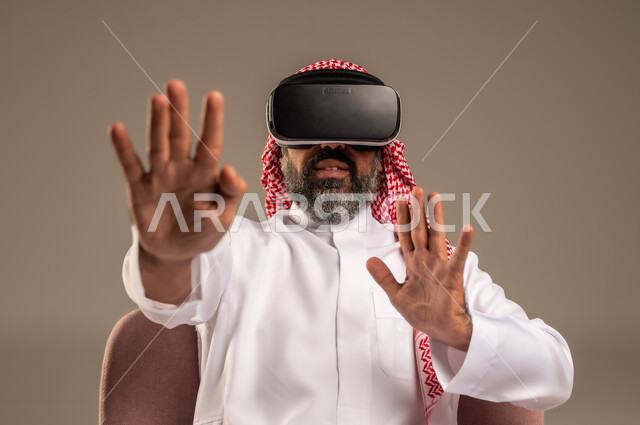 قضاء أوقات ممتعة ومسلية بالألعاب الافتراضية، الاستمتاع بمشاهدة أفلام الواقع الافتراضي، بورتريه لرجل عربي خليجي سعودي كبير بالسن يرتدي الثوب التقليدي و الشماغ يجلس على كرسي مريح ويرتدي نظارة الواقع الافتراضي ثلاثية الابعاد،  خلفية بيج