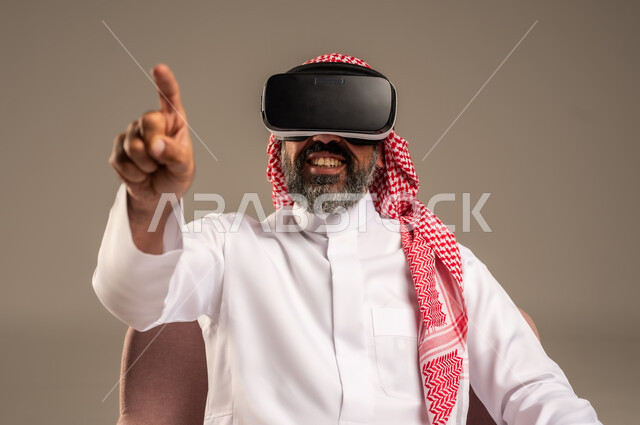 قضاء أوقات ممتعة ومسلية بالألعاب الافتراضية، الاستمتاع بمشاهدة أفلام الواقع الافتراضي، بورتريه لرجل عربي خليجي سعودي كبير بالسن يرتدي الثوب التقليدي و الشماغ يجلس على كرسي مريح ويرتدي نظارة الواقع الافتراضي ثلاثية الابعاد،  خلفية بيج