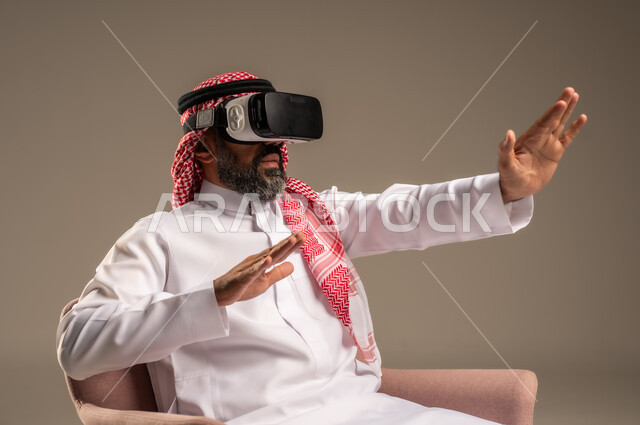 قضاء أوقات ممتعة ومسلية بالألعاب الافتراضية، الاستمتاع بمشاهدة أفلام الواقع الافتراضي، بورتريه لرجل عربي خليجي سعودي كبير بالسن يرتدي الثوب التقليدي و الشماغ يجلس على كرسي مريح ويرتدي نظارة الواقع الافتراضي ثلاثية الابعاد،  خلفية بيج