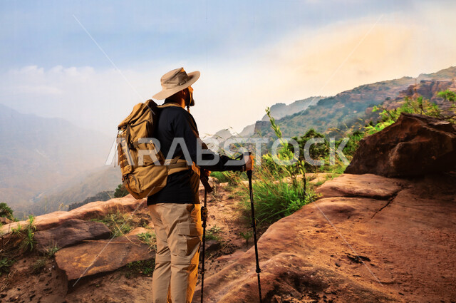 Recreational physical activities, tours and camping trips in Saudi Arabia, maintaining health and fitness, back view of a young Saudi Arabian Gulf man wearing a mountain climbing equipment bag, practicing hiking, mountain peaks and heights