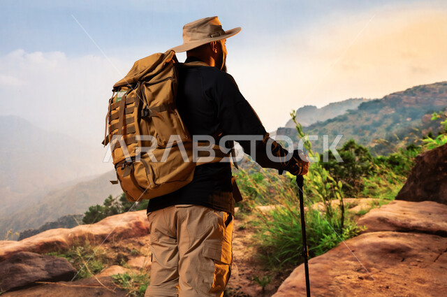  انشطة بدنية ترفيهية، جولات ورحلات التخييم في السعودية, الحفاظ على الصحة واللياقة, صورة من الخلف لشاب عربي خليجي سعودي يرتدي حقيبة معدات تسلق الجبال, ممارسة رياضة الهايكنج، قمم ومرتفعات جبلية