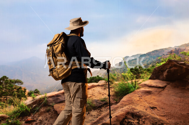 Recreational physical activities, tours and camping trips in Saudi Arabia, maintaining health and fitness, back view of a young Saudi Arabian Gulf man wearing a mountain climbing equipment bag, practicing hiking, mountain peaks and heights