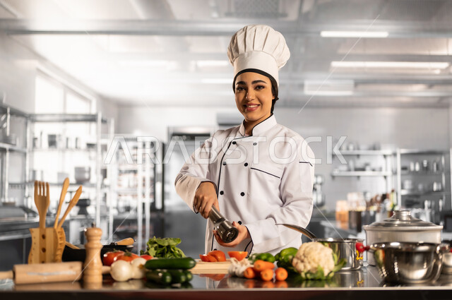 العمل في مطابخ ومطاعم المملكة، فنون ومهارات الطبخ, إعداد الاكل بمكونات طبيعية طازجة، صورة لامرأة عربية خليجية سعودية مبتسمة ترتدي مئزر الطبخ تقوم بإعداد الطعام بايماءات السرور والسعادة، فن الطهي وتحضير الأطعمة اللذيذة، تقديم المأكولات الشعبية التقليدية الشهية