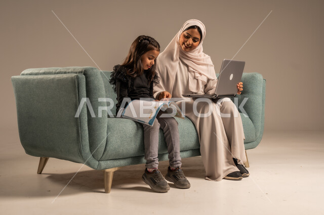 Follow up on e-learning platforms available online, integrating education with technology, solving homework, a private teacher to follow up on lessons at home, a portrait of a veiled Saudi Arabian Gulf mother teaching and educating her daughter using a laptop, gray background