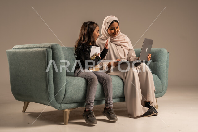 Follow up on e-learning platforms available online, integrating education with technology, solving homework, a private teacher to follow up on lessons at home, a portrait of a veiled Saudi Arabian Gulf mother teaching and educating her daughter using a laptop, gray background