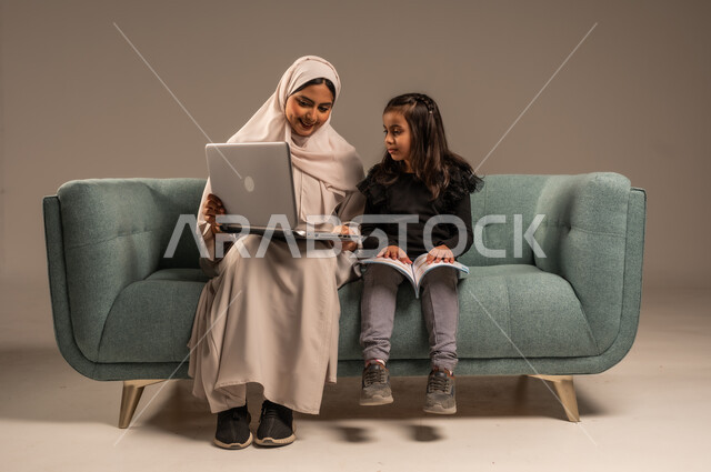  دمج التعليم مع التقنية و التكنولوجيا، حل الواجبات المنزليه، معلمة خصوصي لمتابعة الدروس في المنزل، متابعة منصات التعليم الالكتروني المتاحة عبر الانترنت، بورتريه لأم عربية خليجة سعودية محجبة تقوم بتعليم وتدريس ابنتها باستخدام الحاسب المحمول، خلفية رمادية