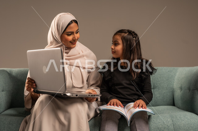  دمج التعليم مع التقنية و التكنولوجيا، حل الواجبات المنزليه، معلمة خصوصي لمتابعة الدروس في المنزل، متابعة منصات التعليم الالكتروني المتاحة عبر الانترنت، بورتريه لأم عربية خليجة سعودية محجبة تقوم بتعليم وتدريس ابنتها باستخدام الحاسب المحمول، خلفية رمادية