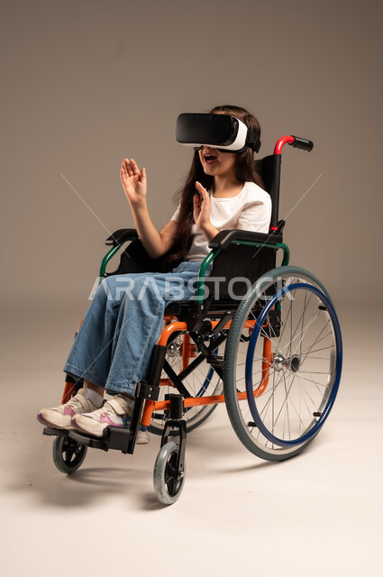  تحسين جودة حياة ذوي الاعاقة الحركية، استخدام كراسي المعاقين للمساعدة على الحركة والتنقل، بورتريه لفتاة عربية  خليجية سعودية ترتدي الزي الكاجوال تقوم بمشاهدة أفلام عبر نظارات الواقع الافتراضي ثلاثية الأبعاد، محاكاة العالم الخيالي والتفاعل مع الفيلم، خلفية رمادية