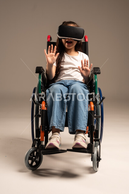  تحسين جودة حياة ذوي الاعاقة الحركية، استخدام كراسي المعاقين للمساعدة على الحركة والتنقل، بورتريه لفتاة عربية  خليجية سعودية ترتدي الزي الكاجوال تقوم بمشاهدة أفلام عبر نظارات الواقع الافتراضي ثلاثية الأبعاد، محاكاة العالم الخيالي والتفاعل مع الفيلم، خلفية رمادية