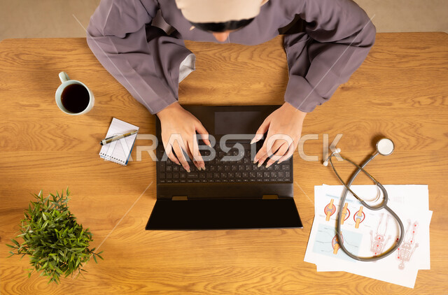 دمج التكنولوجيا في الحياة العملية، مفهوم الطب والرعاية الصحية، الخدمات والأجهزة الطبية، استخدام التقنيات الحديثة والمتطورة، بورتريه علوي عامودي لإمرأة عربية خليجية عمانية تستخدم الهاتف والحاسوب المحمول