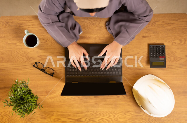 Integrating technology and modern devices into practical life, using a calculator to perform calculations, supervising and auditing engineering projects and plans, working in accounting management, vertical upper portrait of an Omani Gulf Arab woman using a laptop