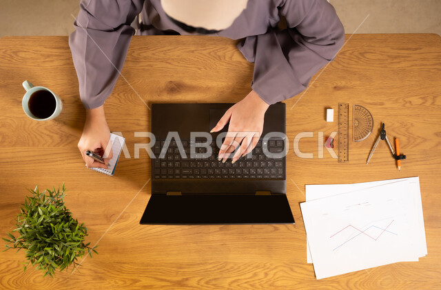 دمج التكنولوجيا في الحياة العلمية، استخدام التقنيات الحديثة والمتطورة، تعلم الحساب والرياضيات من خلال المواقع الالكترونية، التدريب الحسابي عن طريق الاونلاين، بورتريه علوي عامودي لإمرأة عربية خليجية عمانية تستخدم الحاسوب المحمول وتقوم بتدوين الملاحظات