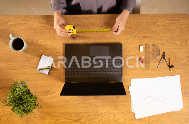 التدريب الحسابي عن طريق الاونلاين، استخدام التقنيات الحديثة والمتطورة، تعلم الحساب والرياضيات من خلال المواقع الالكترونية، دمج التكنولوجيا في الحياة العلمية، بورتريه علوي عامودي لإمرأة عربية خليجية عمانية تستخدم الحاسوب المحمول وتحمل بيدها المتر