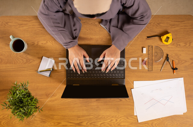 تعلم الحساب والرياضيات من خلال المواقع الالكترونية، استخدام التقنيات الحديثة والمتطورة، التدريب الحسابي عن طريق الاونلاين، دمج التكنولوجيا في الحياة العلمية، بورتريه علوي عامودي لإمرأة عربية خليجية عمانية تستخدم الحاسوب المحمول وبجانبها الأدوات الهندسية