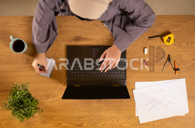 Using modern and advanced technologies, learning arithmetic and mathematics through websites, online arithmetic training, integrating technology into scientific life, vertical upper portrait of an Arab Gulf Omani woman using a laptop and taking notes