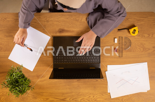Integrating technology into scientific life, learning arithmetic and mathematics through websites, online arithmetic training, using modern and advanced technologies, vertical upper portrait of an Arab Gulf Omani woman using a laptop and drawing charts
